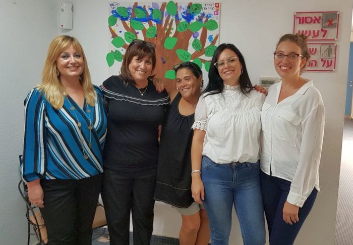 נעמי בצילום משותף עם 4 נשים מחובקות ברקע ציור קיר של עץ