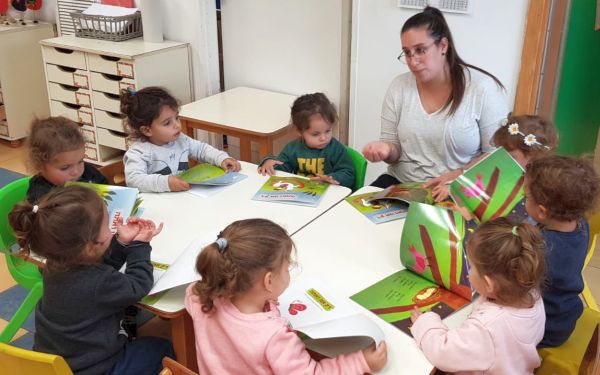ילדים וגננת סביב שולחן קוראים ספרים