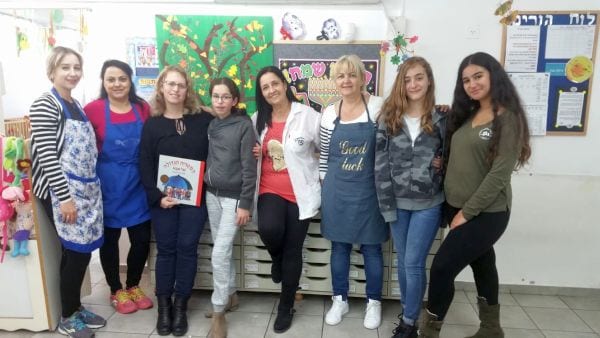 חמש נשות צוות בתמונה משותפת עם שלוש נערות מתנדבות מחייכות למצלמה מחובקות
