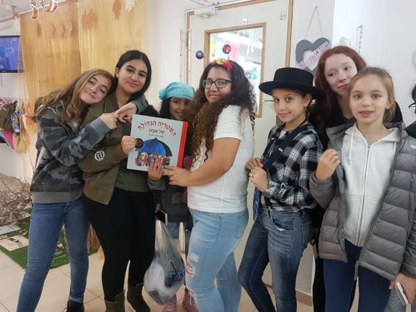 8 נערות עומדות מול המצלמה מחזיקות ספר