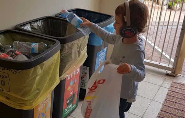 ילד עם אוזניות מחזיק שקית ומעביר בקבוקי פלסטיק למחזורית