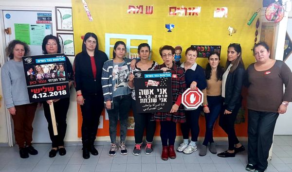 נשים עומדות על רקע קיר שעליו כתוב חנוכה שמח לשתיים מהן יש שלט ביד לעצור את האלימות נגד שנים אחת מחזיקה שלט עצור