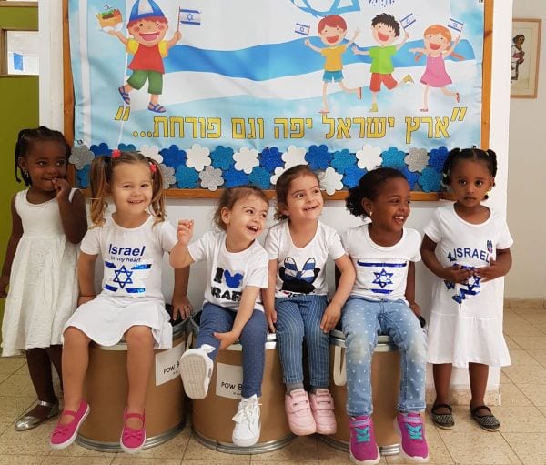 ילדים יושבים בכחול לבן ליד כרזה של יום העצמאות