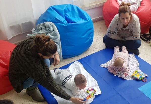 שתי מטפלות על הרצפה מלוות שני תינוקות על מזרן כחול